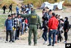 امریکہ اور میکسیکو سرحد کے قریب ڈبل فینس کے ساتھ پناہ کے متلاشیوں کو ایک امریکی بارڈر کنٹرول ایجنٹ ہدایات دے رہا ہے ، فوٹو اےپی 8 مئی 2023