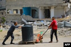دو فلسطینی بمباری سے تباہ ہونے والے مکانوں کے قریب سے گزر رہے ہیں۔ وہ اپنے ساتھ پانی ایک ٹینکر لے جا رہے ہیں۔ 28 مارچ 2024